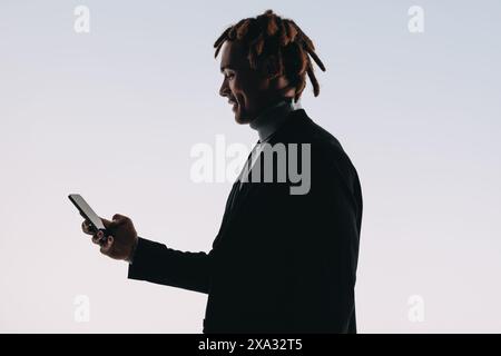 Happy man using a smartphone, reading and texting on a mobile app. Silhouette of a young man highlighting the modern lifestyle of seamless connection Stock Photo