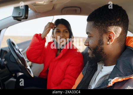 Beautiful happy young loving couple holding hands and smiling while sitting in their first car. Buy your first car concept Stock Photo