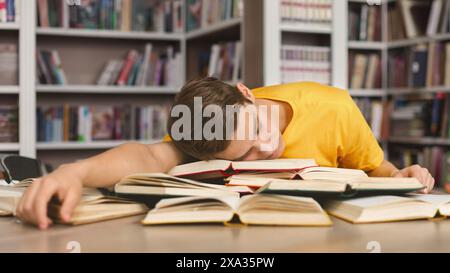 Tired guy napping on books in library Stock Photo