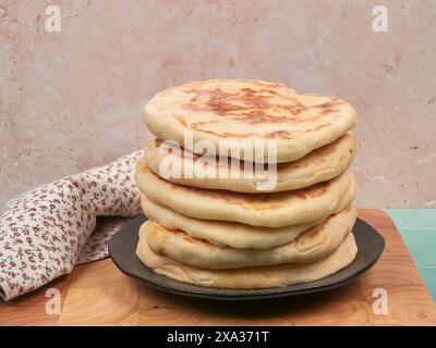 Homemade flatbreads, placed on a brown ceramic plate, on a wooden chopping board set on a green ceramic countertop, with a sandy background Stock Photo