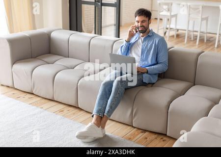 Man Uses Laptop and Cell Phone While Sitting on Sofa Stock Photo