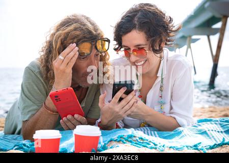 Smiling couple on the beach browsing smartphone apps. Stock Photo
