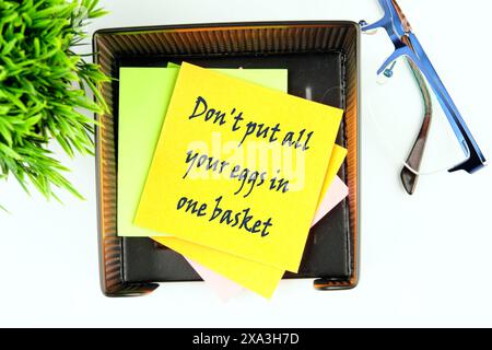 Don't put all your eggs in one basket text on a yellow sticker in a stand on a white background, top view Stock Photo