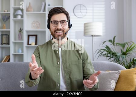 A smiling man with a headset having a video call while sitting in his home office. Remote work and virtual communication concept. Stock Photo