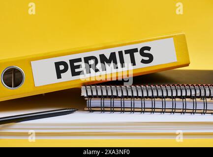 The word permits written on the label of a yellow binder on the office desk. Stock Photo