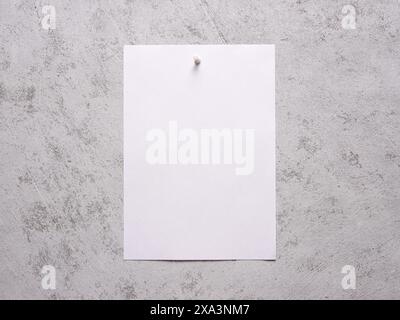 Blank white sheet of paper pinned to a white concrete wall. Stock Photo