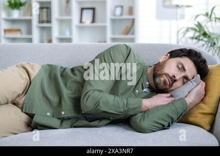Man taking a nap on a comfortable couch in a well-lit living room. Relaxation and rest in a cozy home environment. Stock Photo