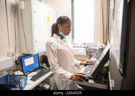 Female technician operating advanced machinery in a medical practice, UK Stock Photo