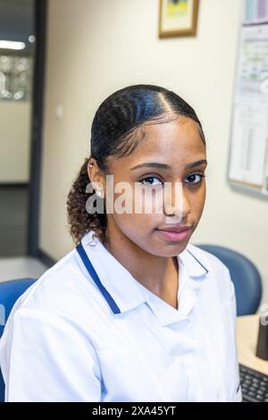 Nurse sitting at a desk with a computer in a medical practice, UK Stock Photo