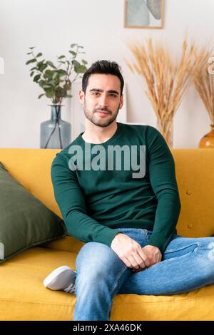 Man sitting on a yellow sofa with crossed legs. Stock Photo