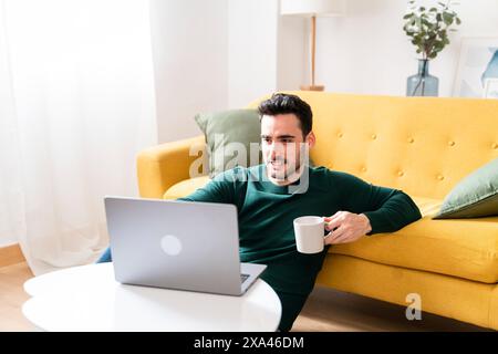 Man with laptop and coffee on yellow sofa. Stock Photo