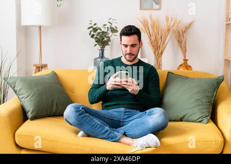 Man using smartphone on a yellow sofa Stock Photo