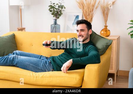 Man relaxing on a yellow sofa holding a remote control Stock Photo