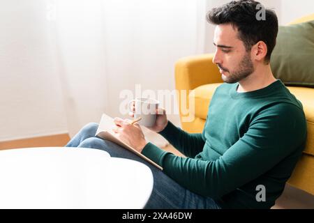 Man making notes and holding a mug on a yellow couch. Stock Photo