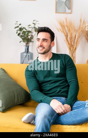 Smiling man sitting on a yellow couch in a cozy living room. Stock Photo