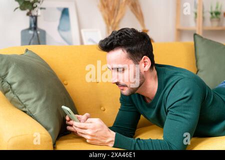 Man intently looking at his smartphone on a yellow couch Stock Photo