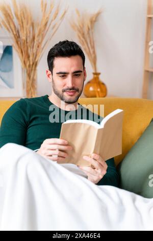 Man reading a book on a yellow sofa Stock Photo