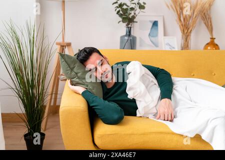 Man resting on a yellow couch with a white blanket Stock Photo
