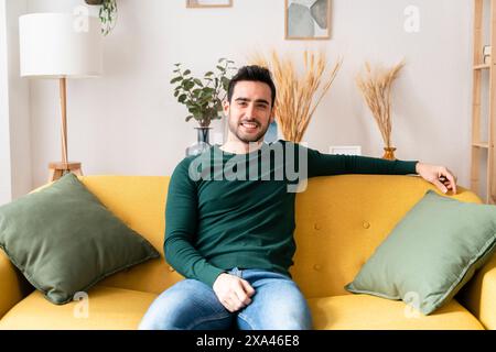 Smiling man sitting comfortably on a yellow couch Stock Photo
