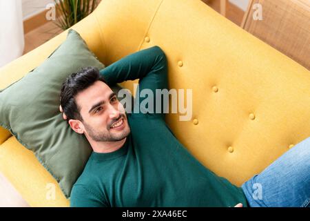 Man relaxing on a yellow sofa with a green pillow Stock Photo
