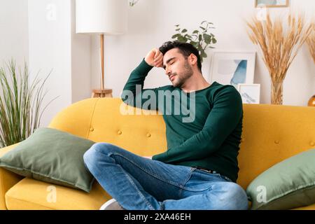 Man sitting on a yellow couch with his eyes closed and hand on forehead Stock Photo