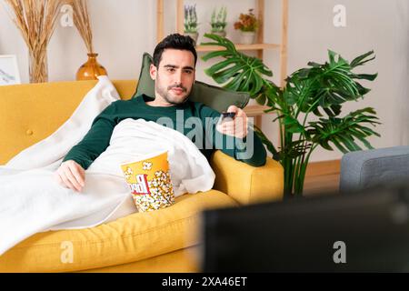Man relaxing on couch with popcorn and remote control. Stock Photo