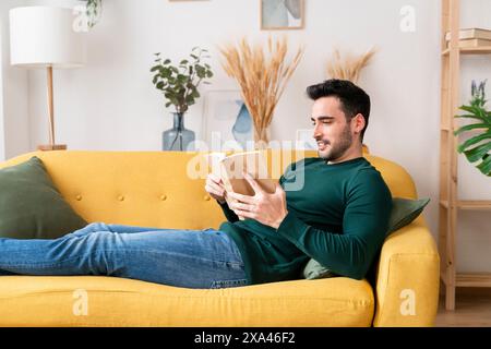 Man reading a book on a yellow sofa. Stock Photo