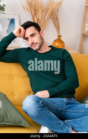 Man seated on a yellow couch in contemplation. Stock Photo