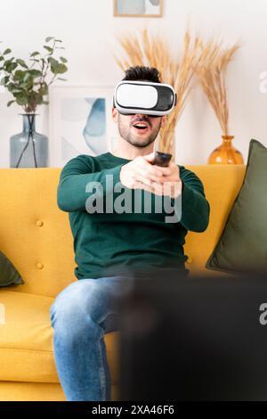 Man using VR AR headset and controller on a yellow sofa Stock Photo
