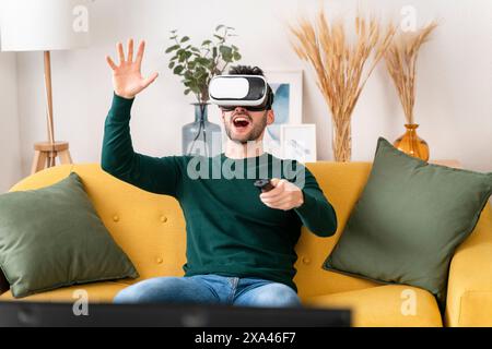 Man using VR AR headset and controller on a yellow sofa Stock Photo
