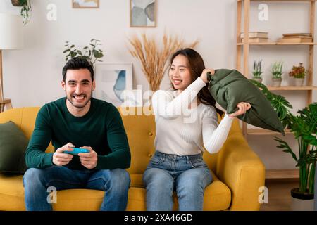 Playful couple on a yellow sofa with a video game controller Stock Photo