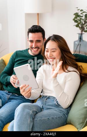 Couple laughing and holding a tablet on a couch. Stock Photo