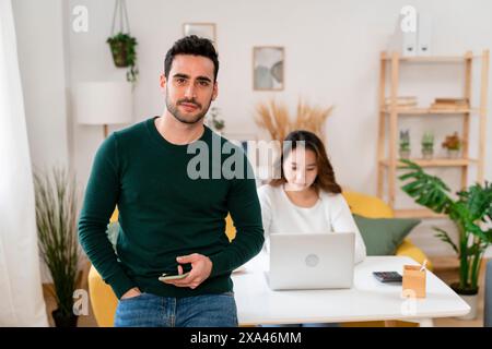 Man standing with phone and woman working on laptop. Stock Photo