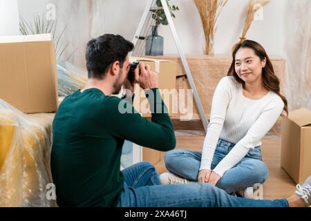 Man takes photo of woman among moving boxes Stock Photo