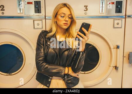 Young Woman in Launderette Using Smartphone Stock Photo