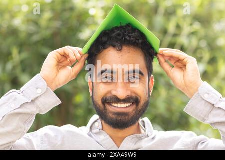 A smiling man holding a green sheet of paper over his head like a roof Stock Photo