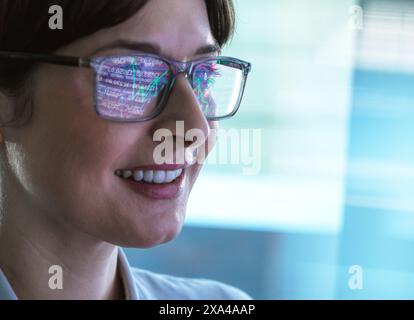 A close-up of a smiling woman wearing glasses that reflect colorful data visualization graphics. Stock Photo