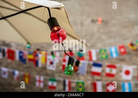 Colored light bulbs are strung in front of a blurred background featuring small international flags hung across a cord. Stock Photo