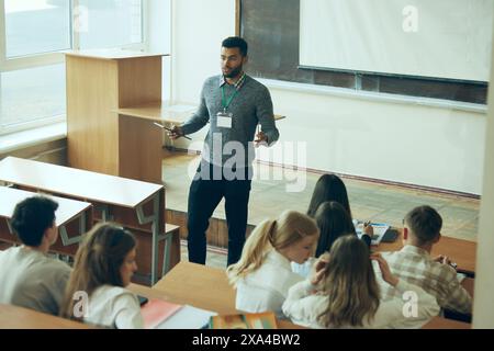 Interactive Learning Session. Young teacher leading lecture in front of classroom, engaging with diverse group of students. Stock Photo