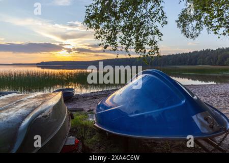 Small plastic rowboats lay head over heels on the lake coast under sunset sky Stock Photo