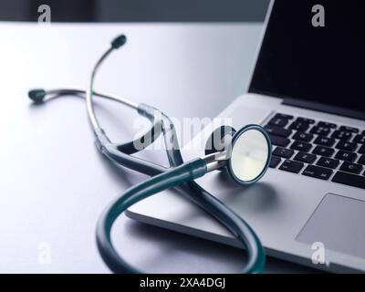 A stethoscope rests on the keyboard of a closed laptop with a silver finish, symbolizing the intersection of healthcare and technology. Stock Photo