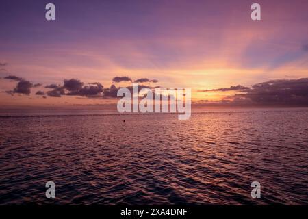 A serene sunset over the ocean with a colorful sky transitioning from vibrant purple to orange hues just above the horizon, reflecting on the water's surface. Stock Photo