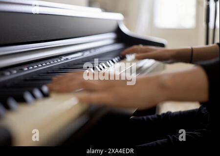 A person is playing a piano, focusing on their hands moving across the black and white keys. Stock Photo