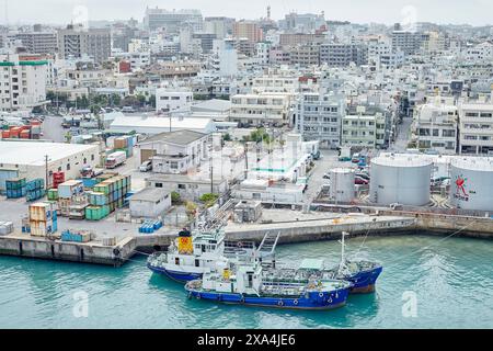 Aerial view of a bustling coastal cityscape with a focus on a docked blue fishing vessel surrounded by industrial equipment and buildings. Stock Photo