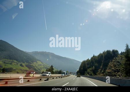 A sunny day view from a car on a highway with mountains, clear blue sky, and lens flare. Stock Photo