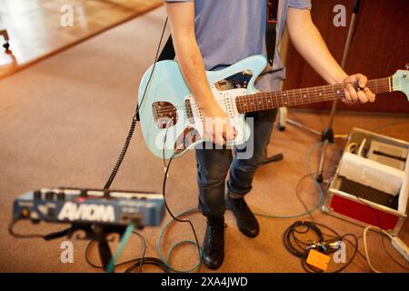 A person standing while playing an electric guitar, surrounded by musical equipment including pedals and an amplifier. Stock Photo