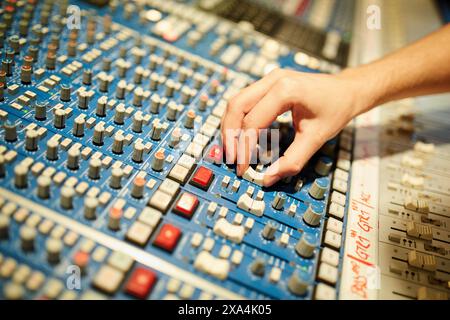 A hand adjusting a knob on a professional audio mixing console with numerous buttons and sliders. Stock Photo