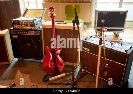 A red electric guitar stands between a microphone and a Vox amplifier in a recording studio, with various audio equipment in the background. Stock Photo