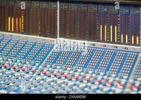 A close-up view of a professional audio mixing console with illuminated level meters displaying sound levels. Stock Photo