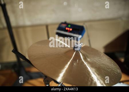 A close-up of a shiny cymbal as part of a drum set with a music amplifier lit by red LEDs in the soft focus background. Stock Photo